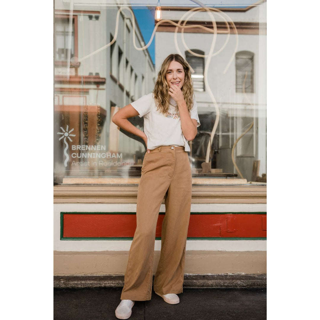 Woman in a white shirt and tan pants standing in front of a store window with 'Brennen Cunningham' branding.