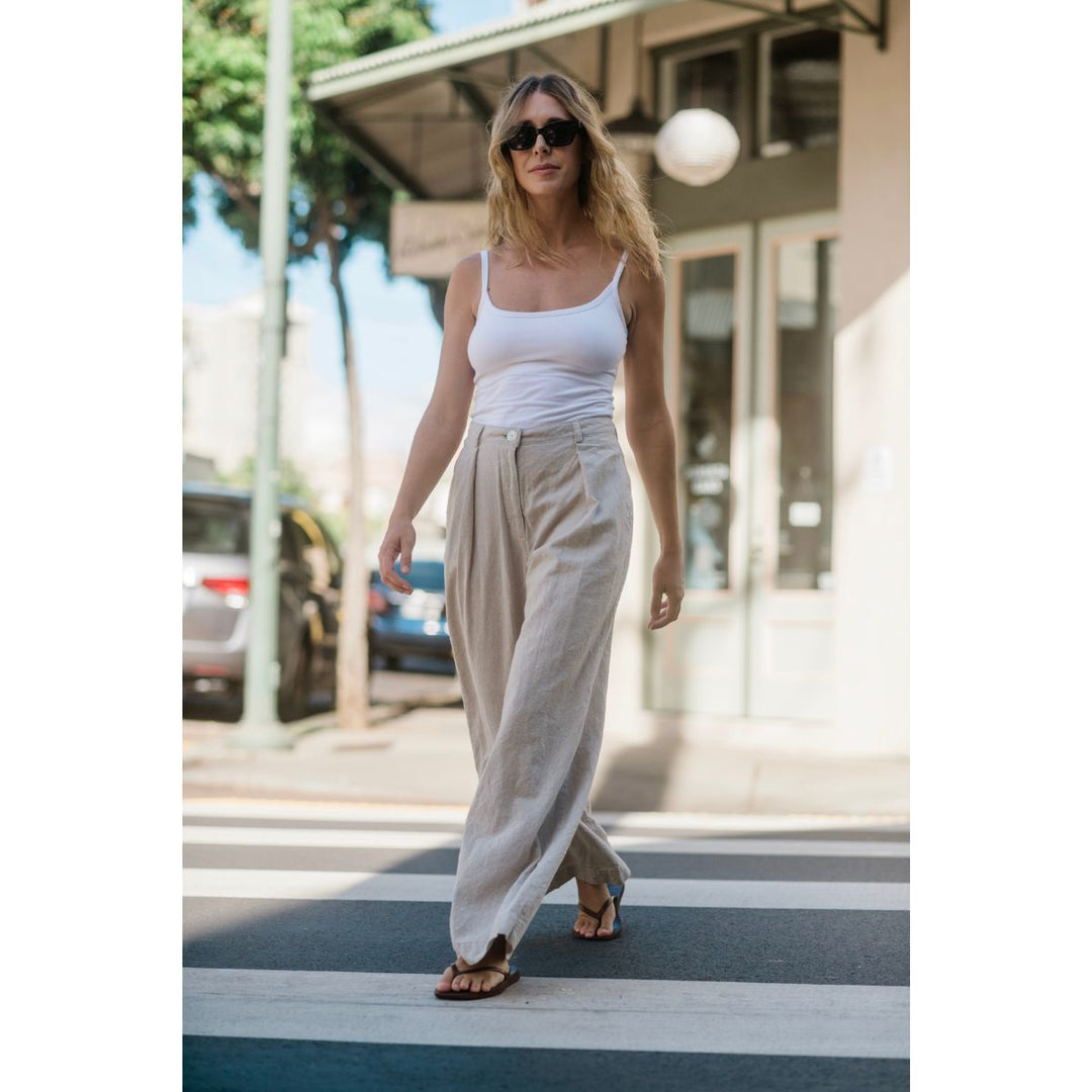 Woman walking on a street wearing a white top and beige pants.