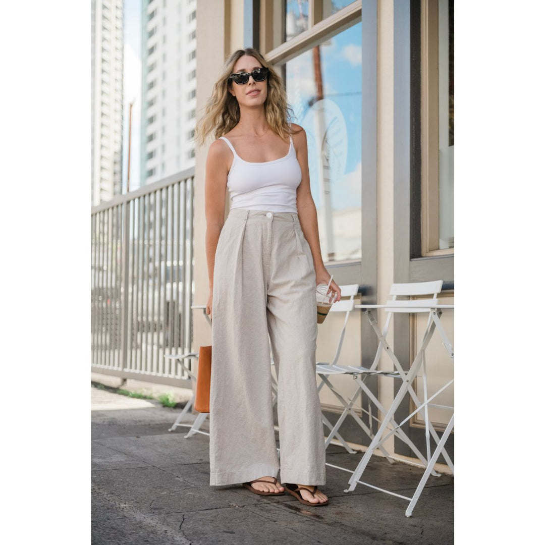 Woman wearing a white tank top and beige wide-leg pants standing on a balcony.