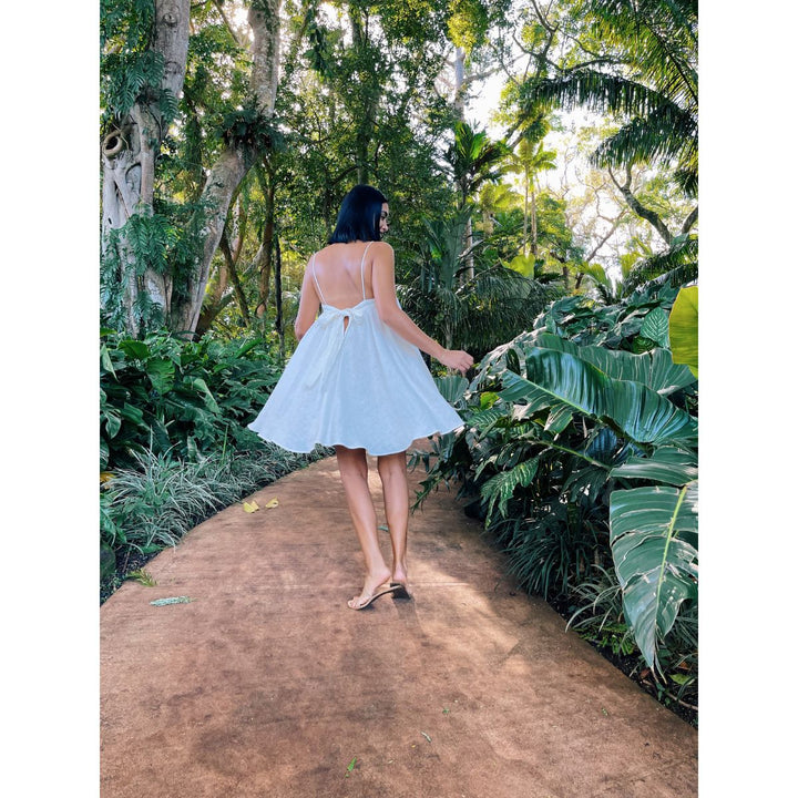 Woman in a light blue dress walking along a dirt path in a lush green forest.