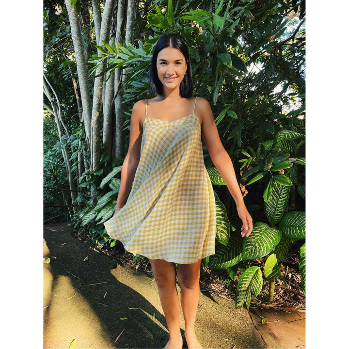 Woman in a yellow checkered dress standing in a lush green garden.