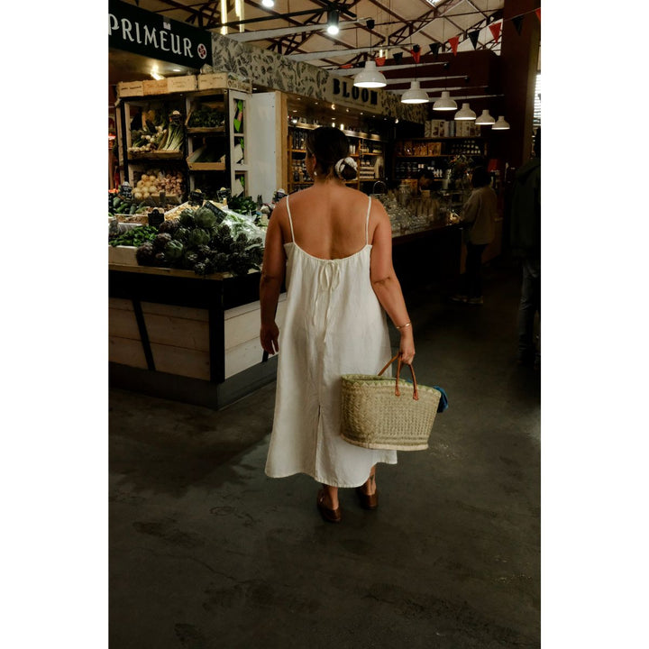 Woman in a white dress holding a basket in a market setting