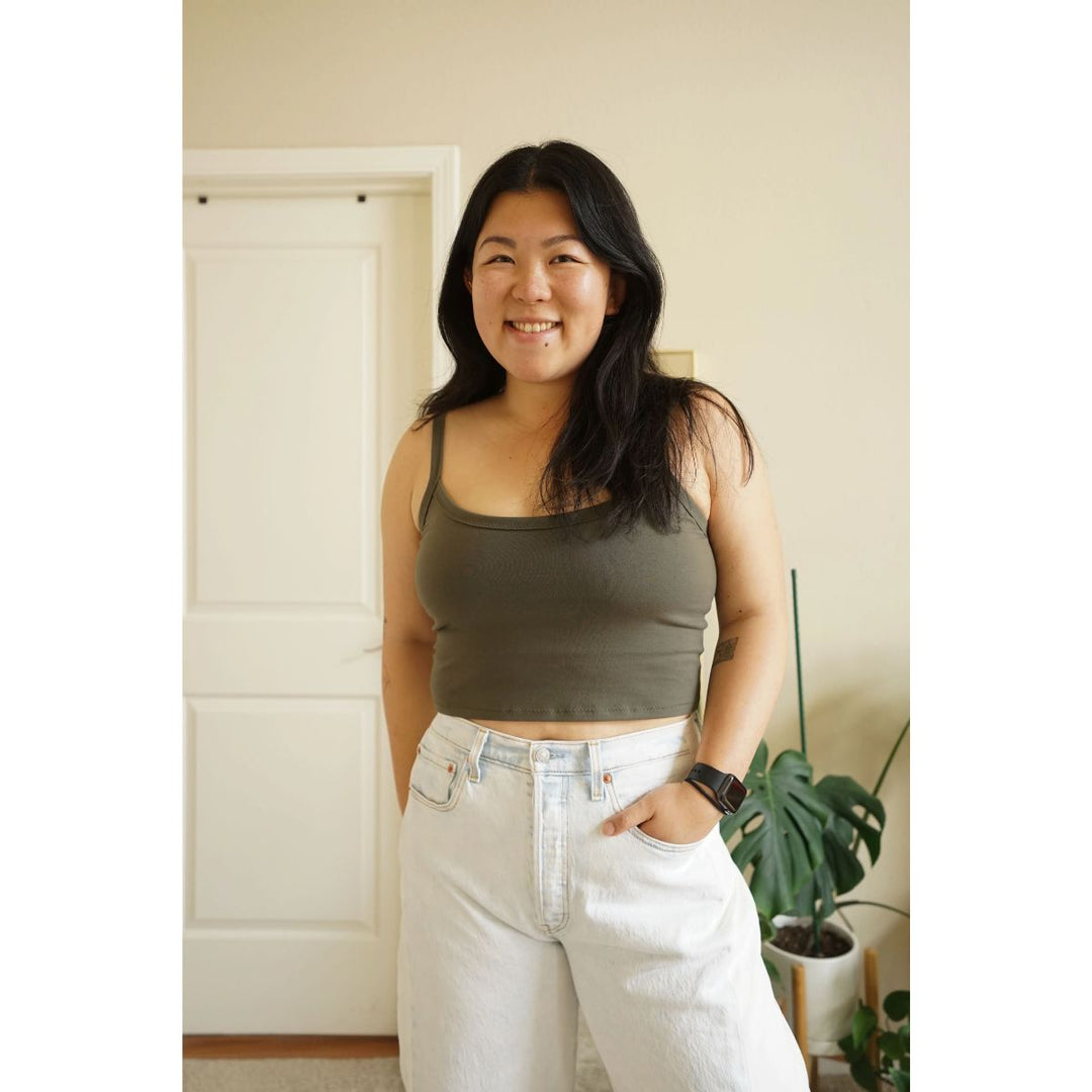Woman wearing a green tank top and white pants standing indoors.
