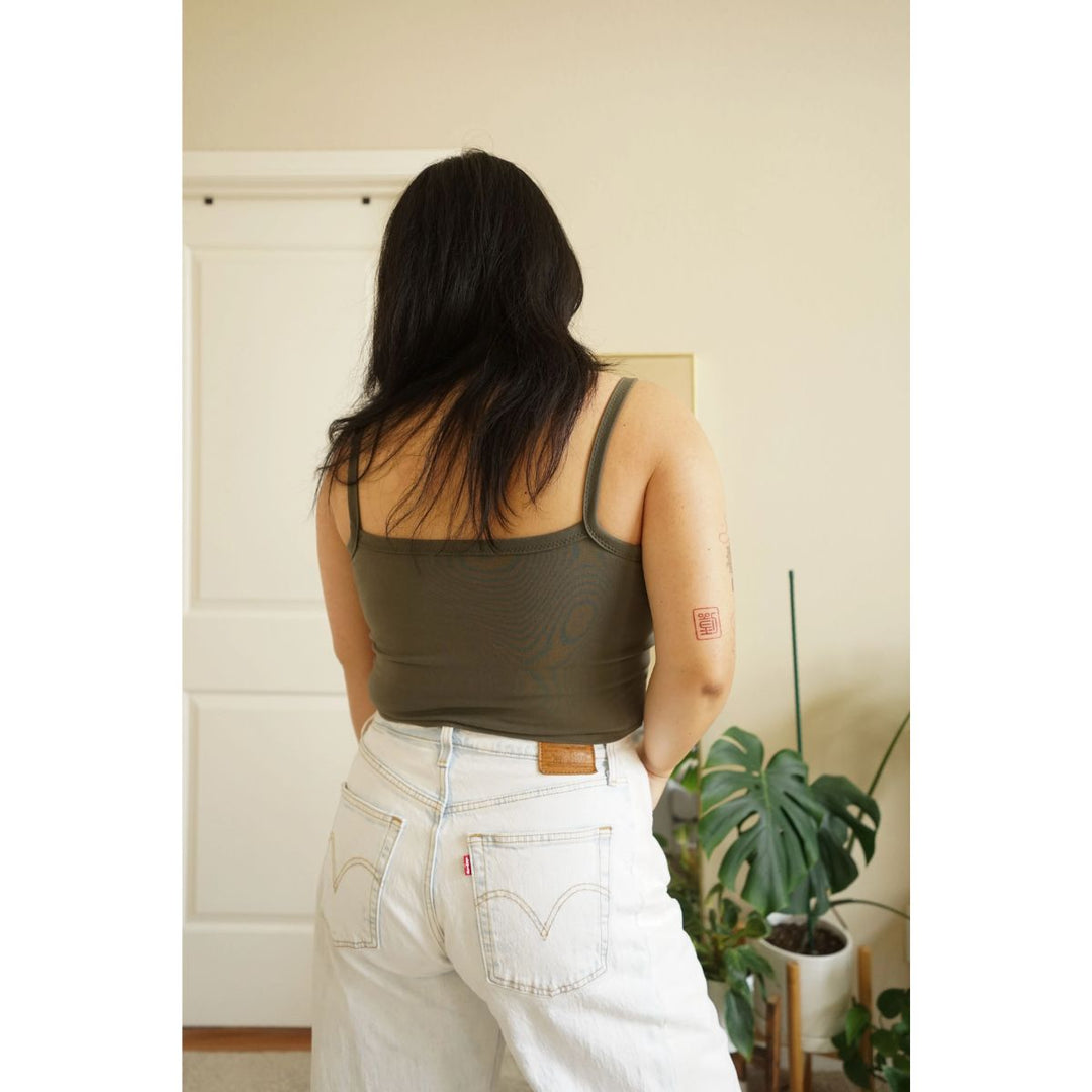 Person wearing a green tank top and white pants in a room with plants.