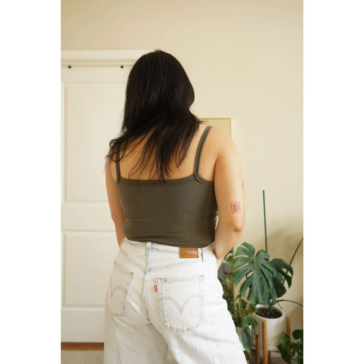 Person wearing a green tank top and white pants in a room with plants.