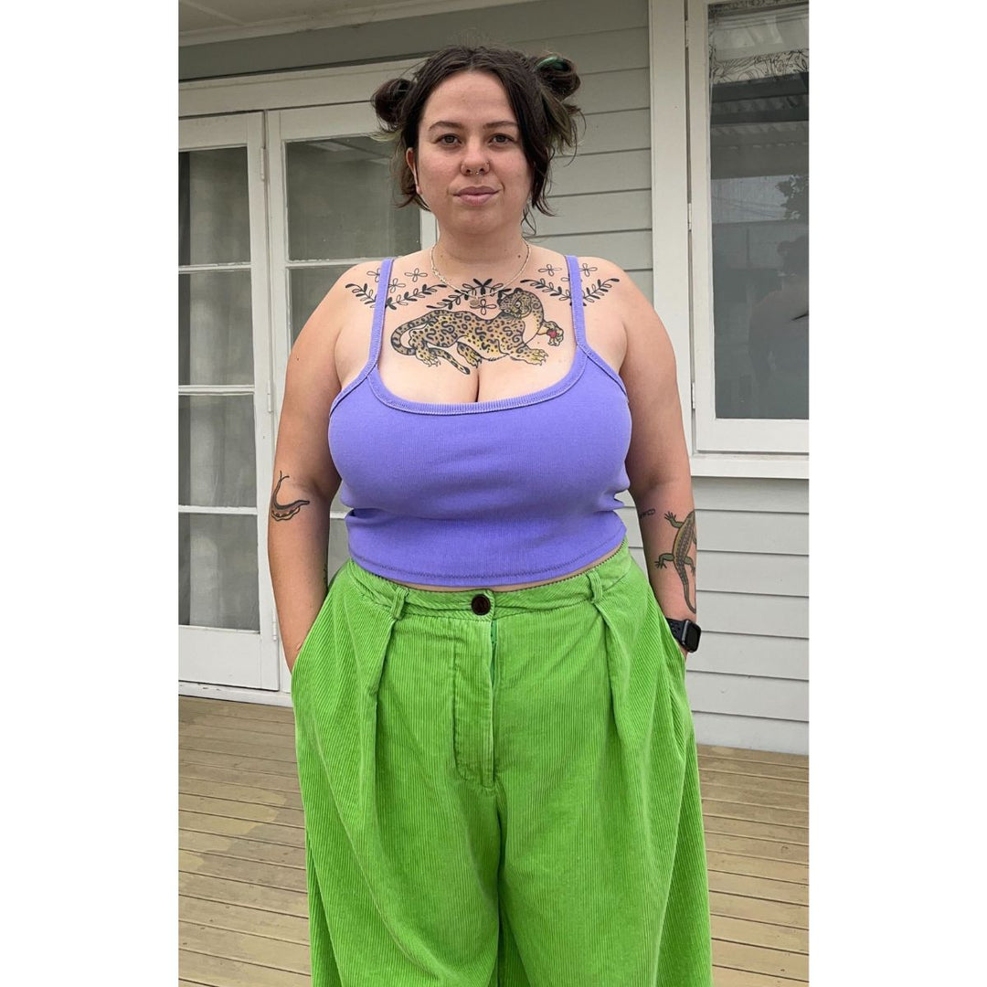 Person wearing a purple tank top and green pants standing outside a house.