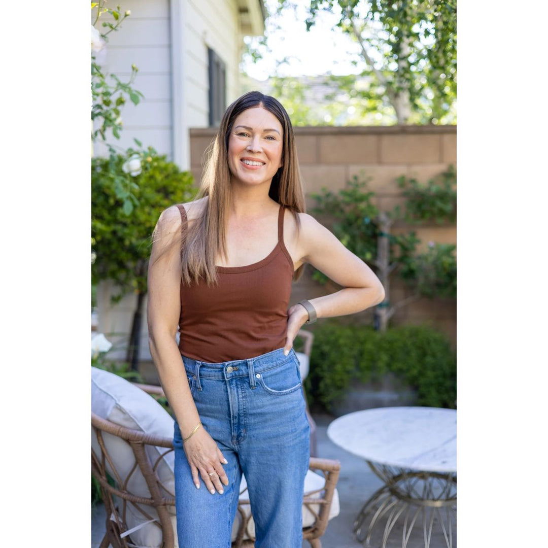 Woman wearing a brown tank top and blue jeans standing outdoors.