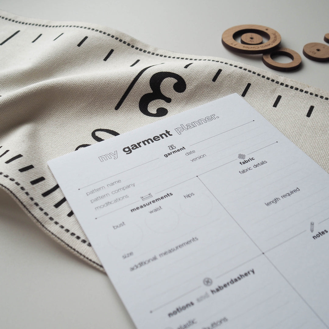 Garment planner sheet on a fabric background with sewing tools.