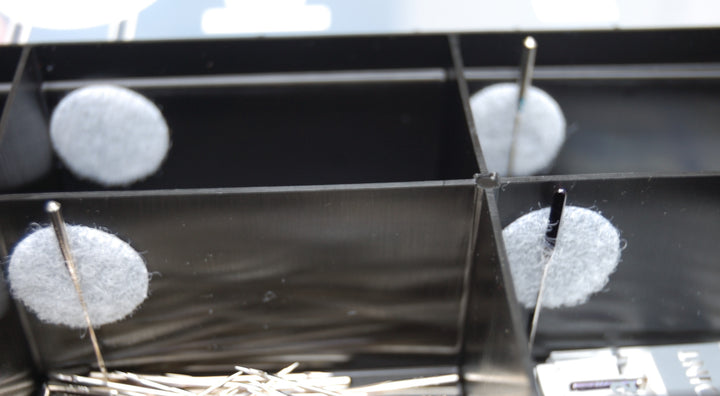 Close-up of a black metal grid with white spherical objects and pins on a blurred background