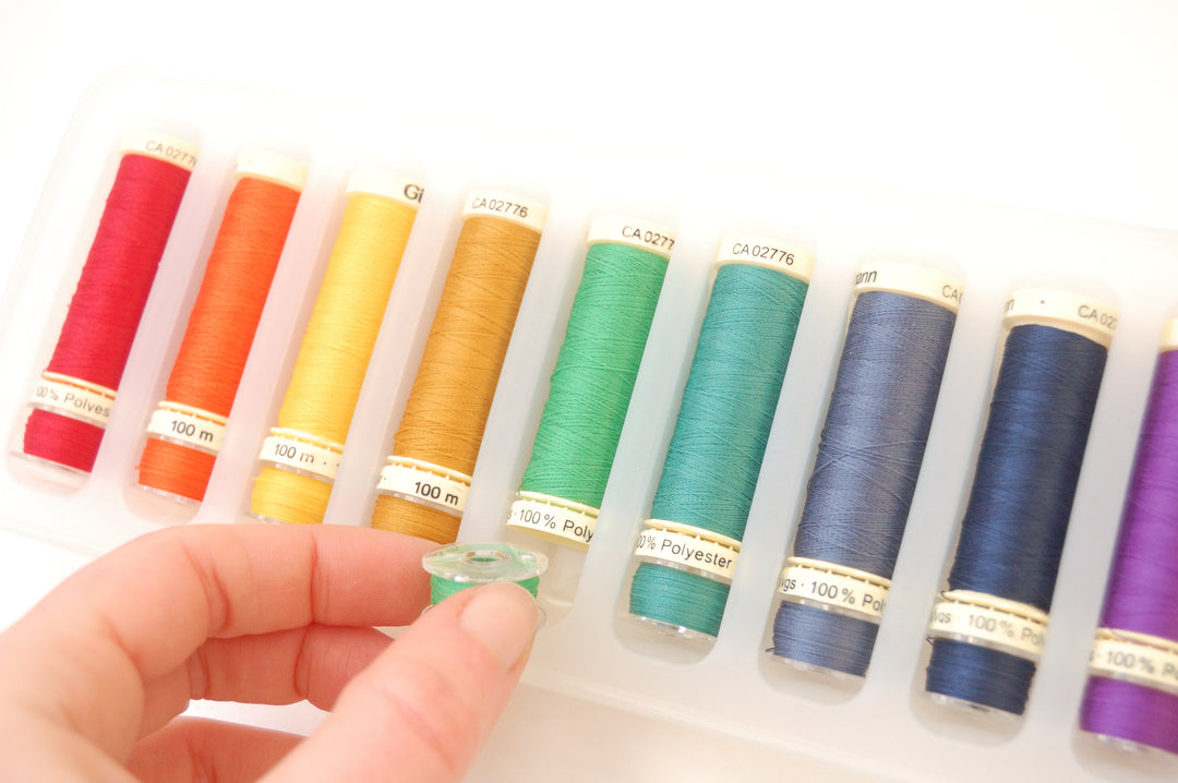 Set of colorful sewing threads in a holder with a hand holding it.