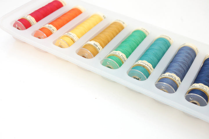 Set of colorful spools of thread in a white tray on a light background