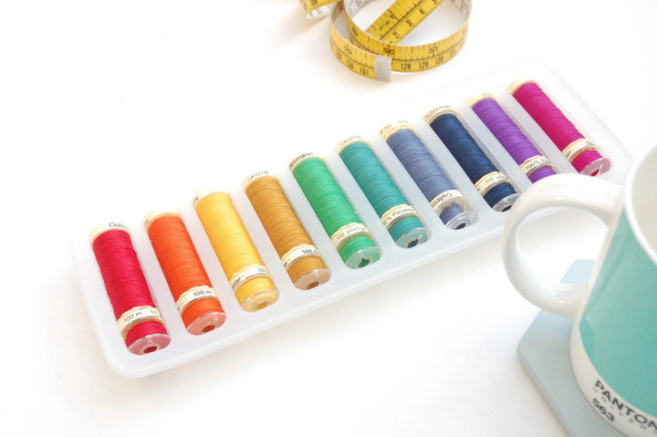Set of colorful spools of thread on a white surface with a measuring tape and mug.