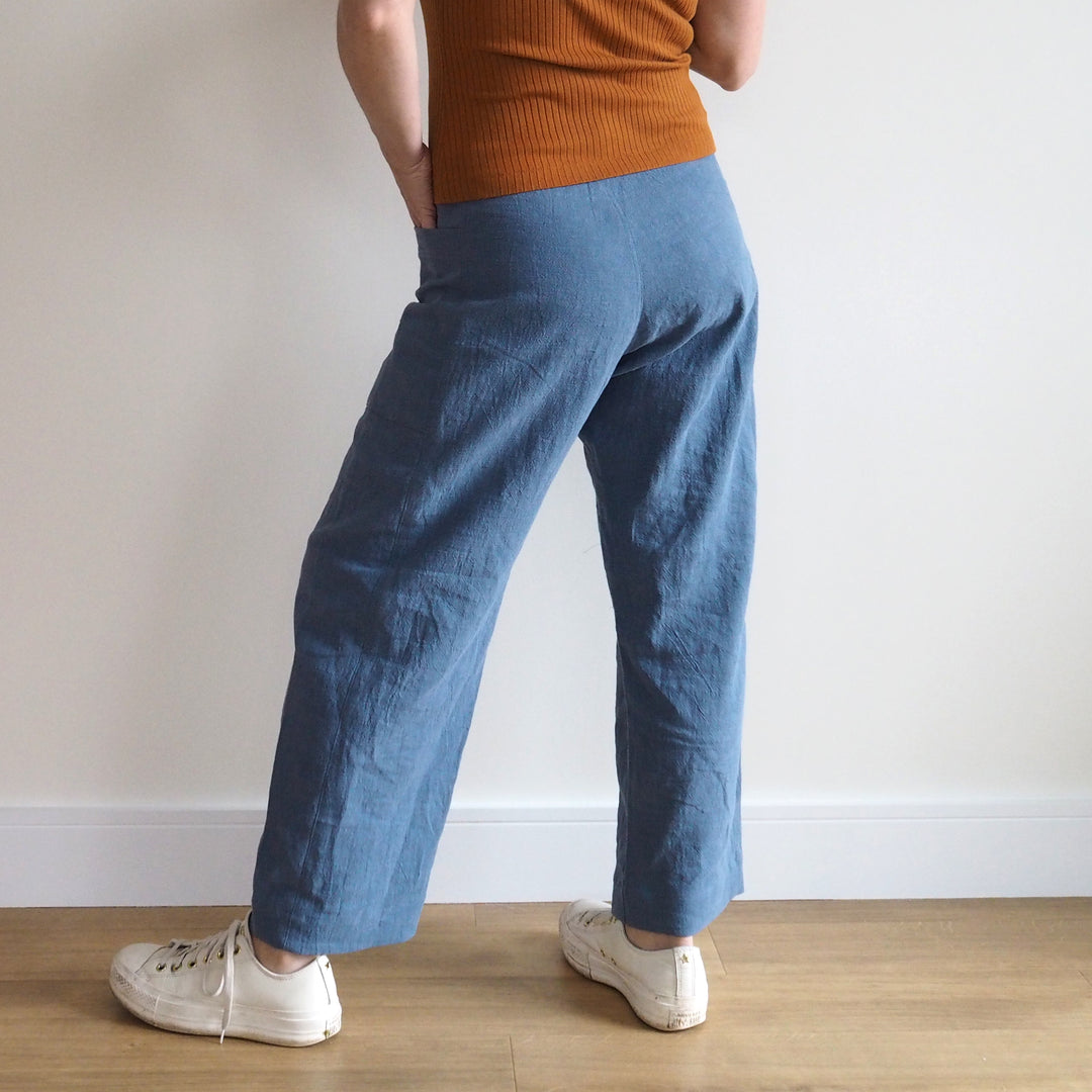 Person wearing blue pants and a brown top standing on a wooden floor with a white wall background