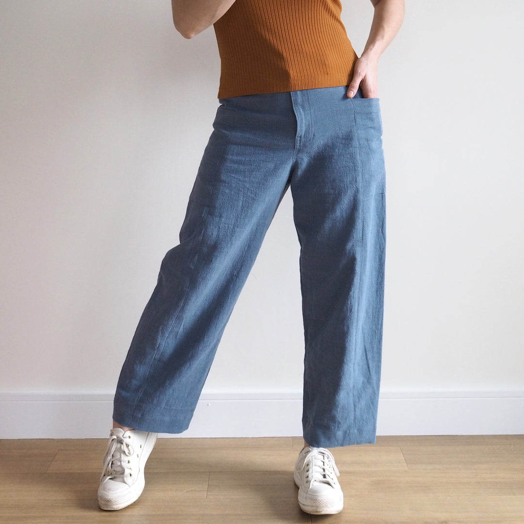 Person wearing blue wide-leg pants and a brown top against a plain background