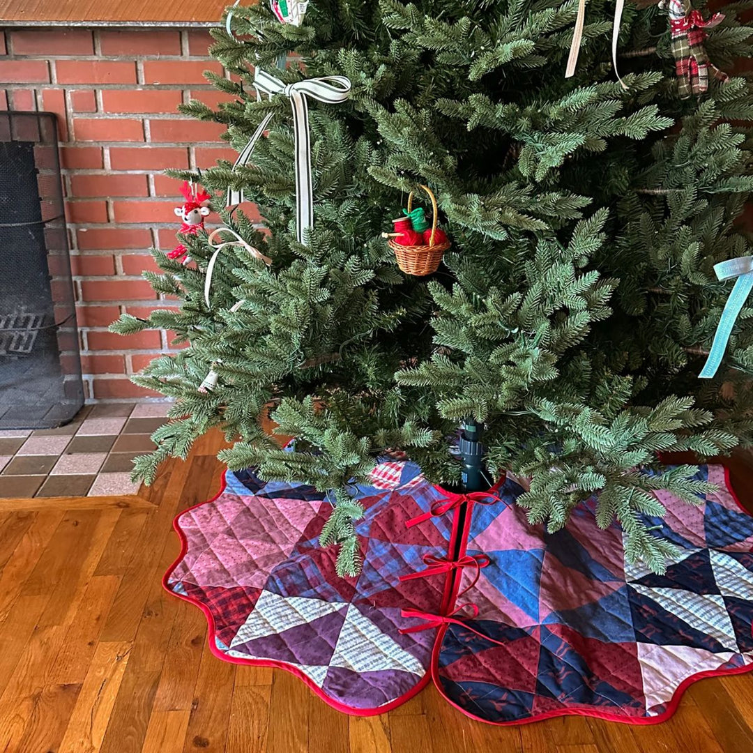 Decorated Christmas tree with a colorful quilted tree skirt in front of a brick fireplace.