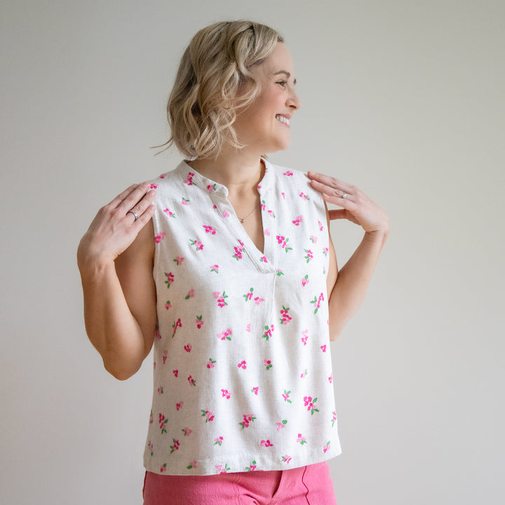 Woman wearing a white sleeveless top with pink floral pattern against a plain background