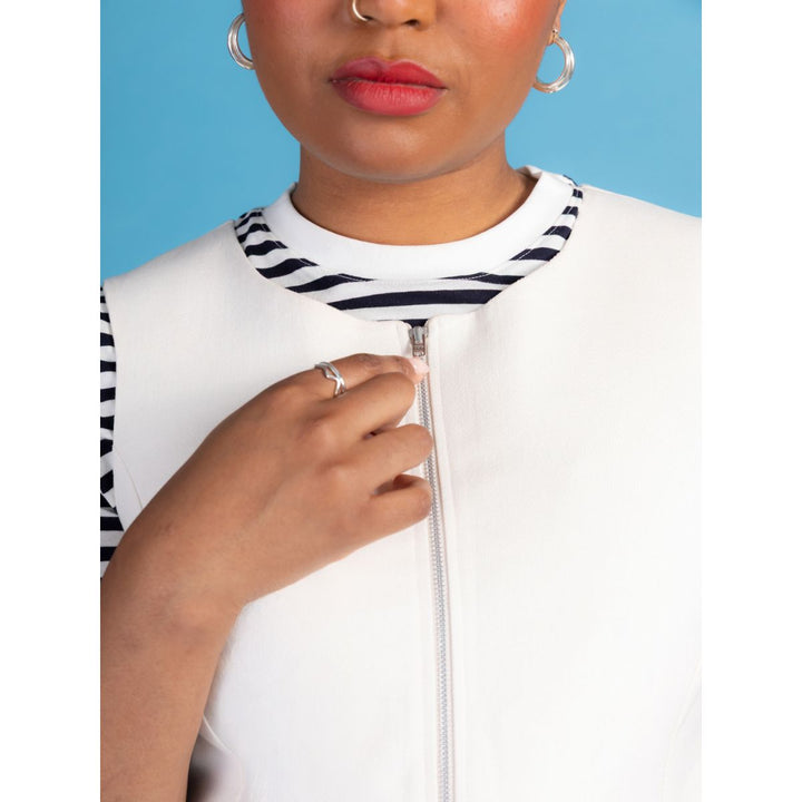 Person wearing a white jacket with a black and white striped collar against a blue background