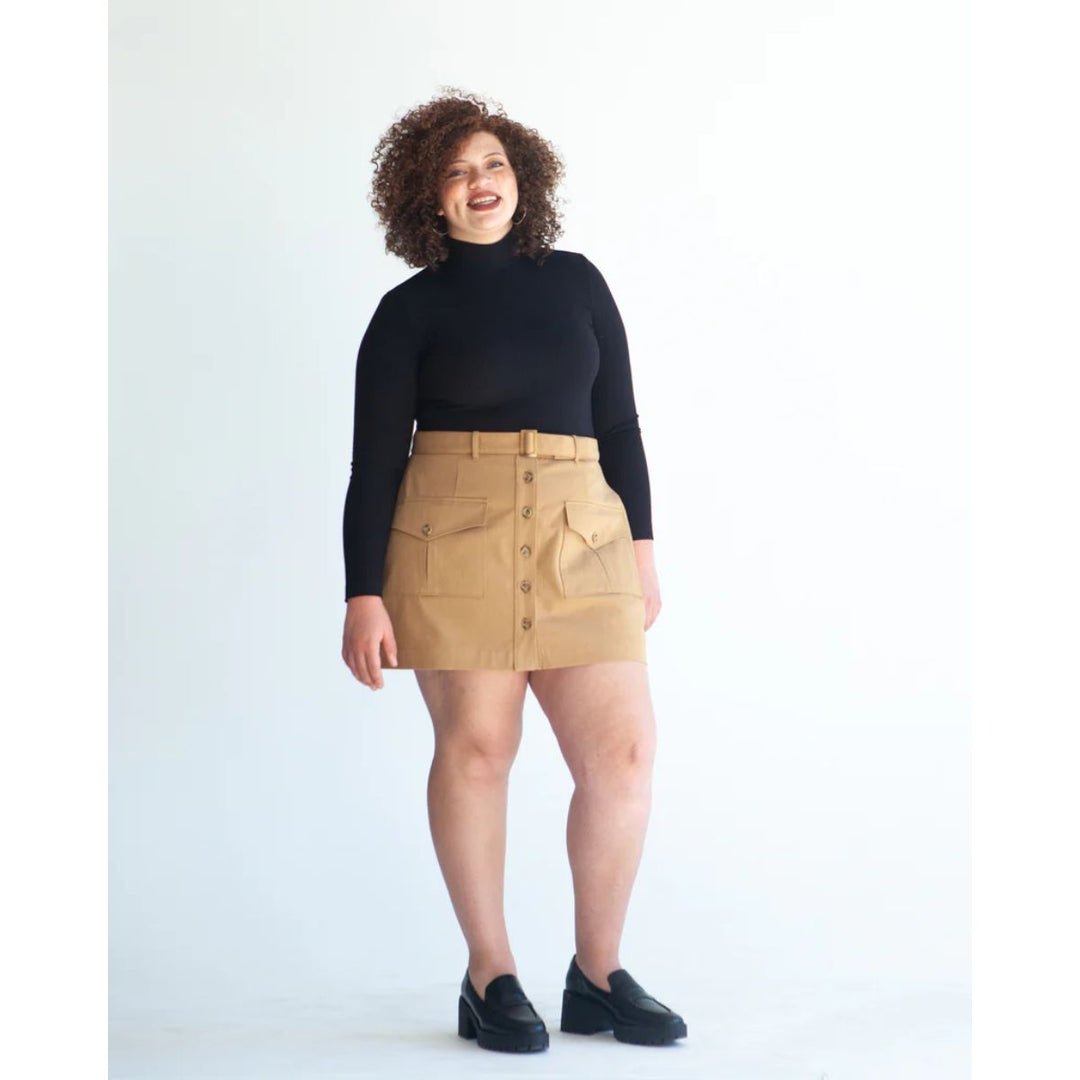 Person wearing a black turtleneck and beige skirt on a white background