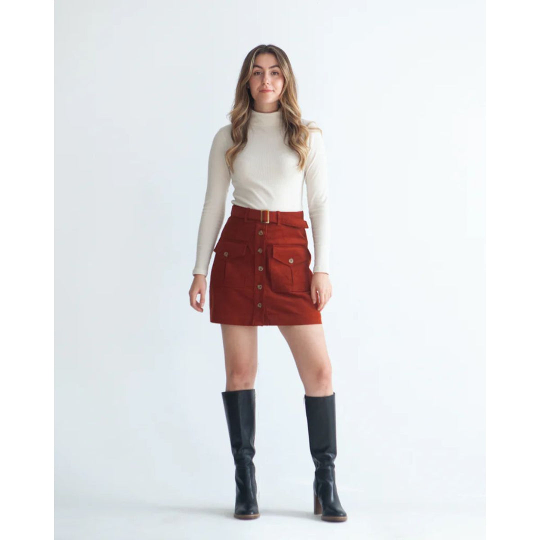 Woman wearing a white turtleneck, red skirt, and black knee-high boots on a white background