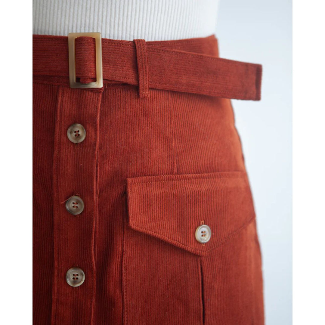 Close-up of a red corduroy skirt with a belt and buttons on a white background