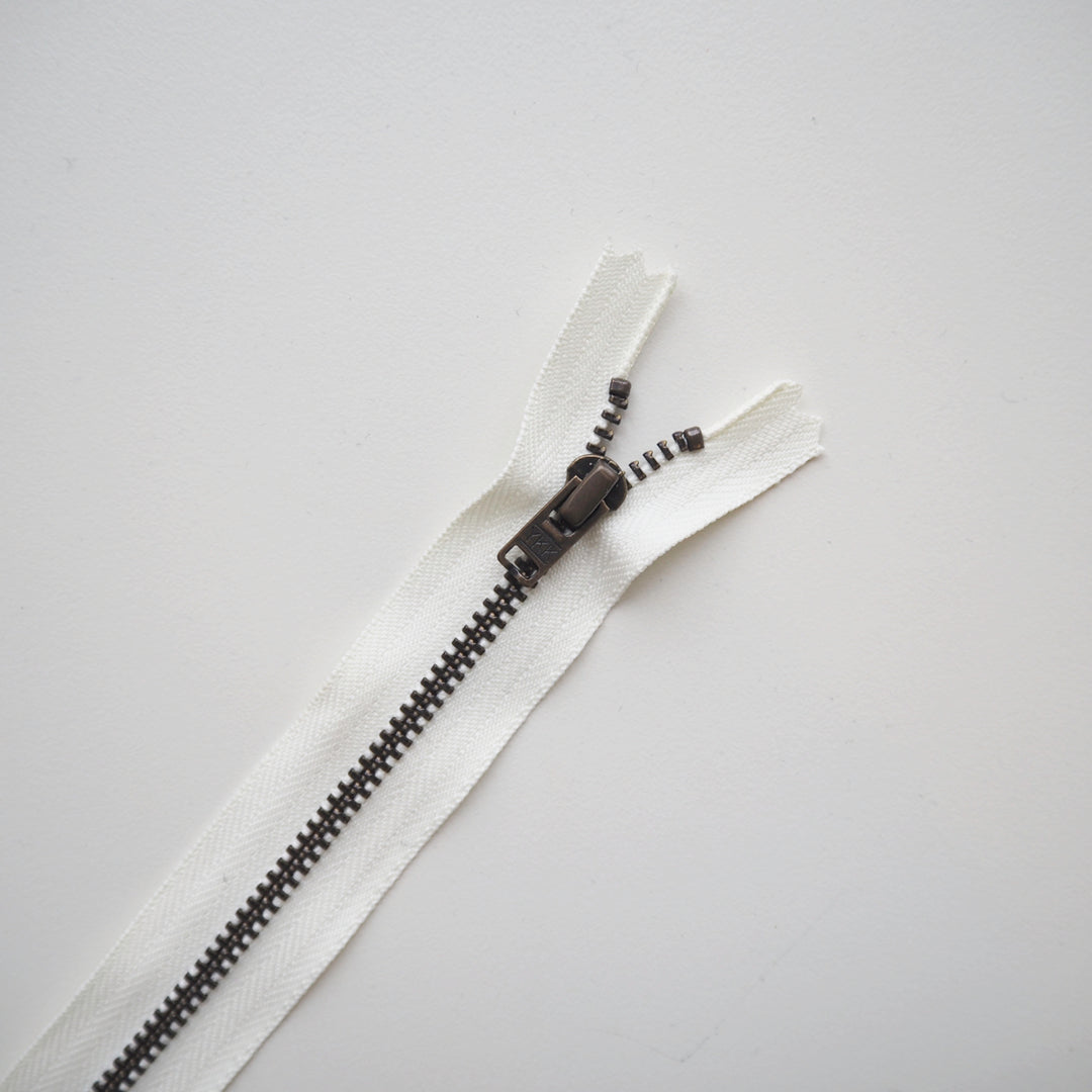 White zipper with brass metal teeth on a grey background