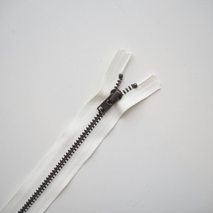 White zipper with brass metal teeth on a grey background