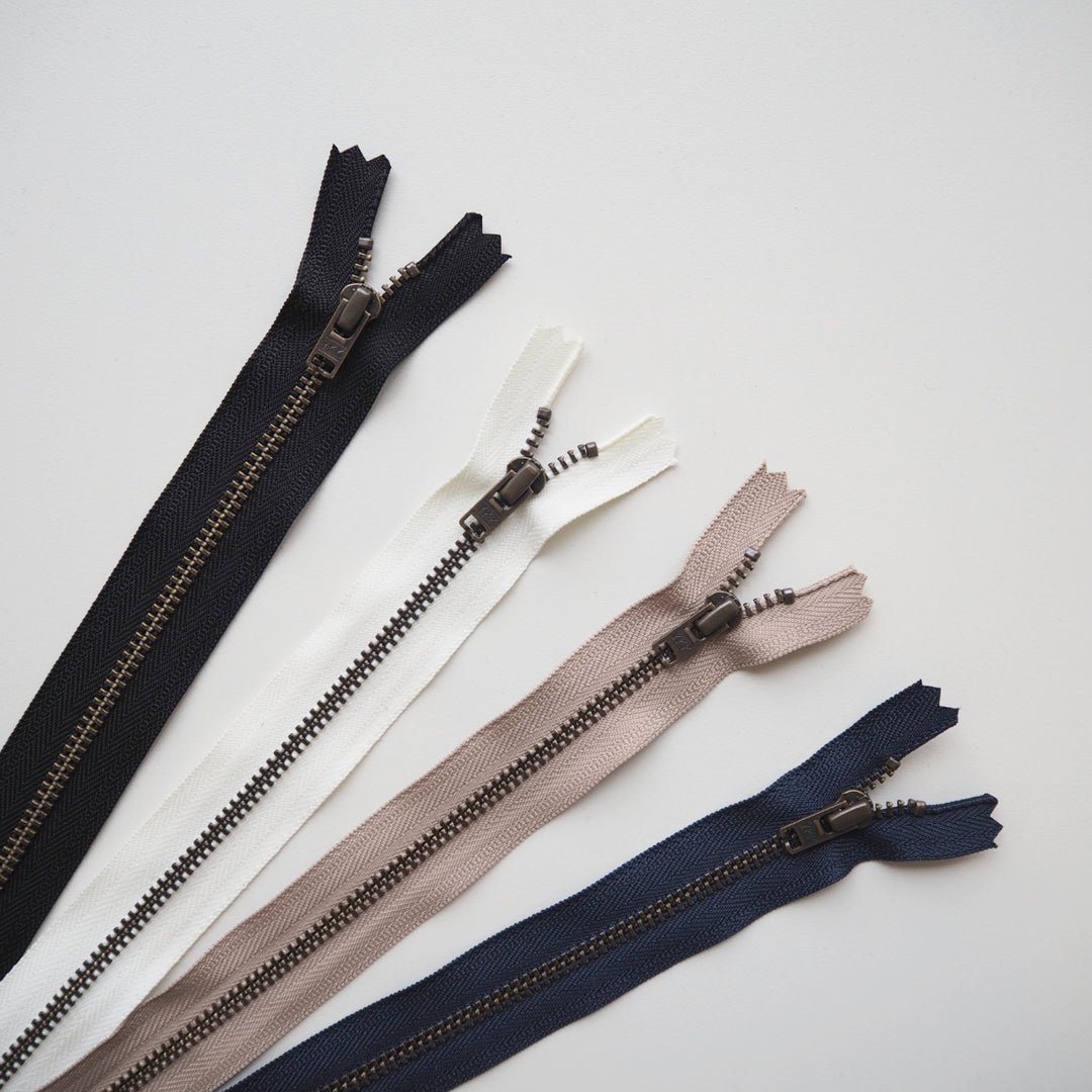 Set of open zippers in black, white, beige, and navy on a light gray background