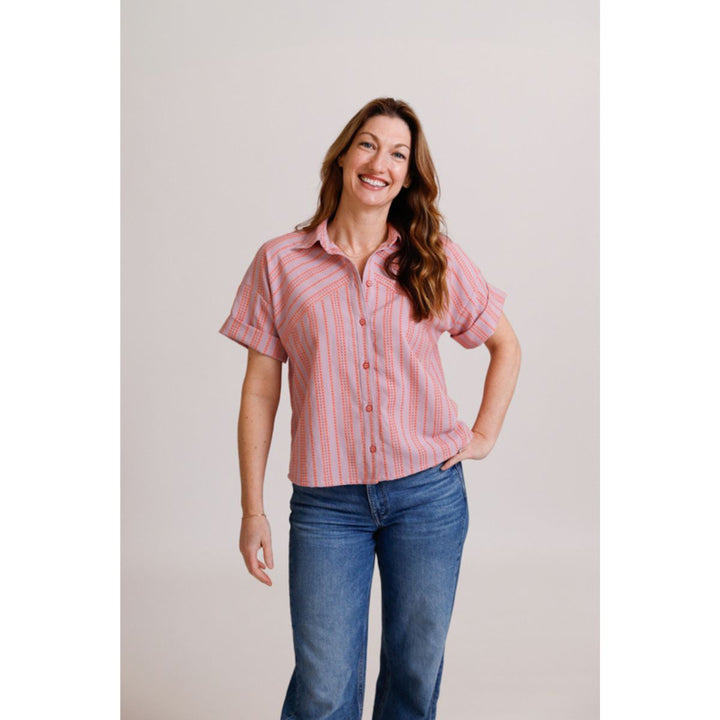 Woman wearing a pink striped shirt and blue jeans against a plain background