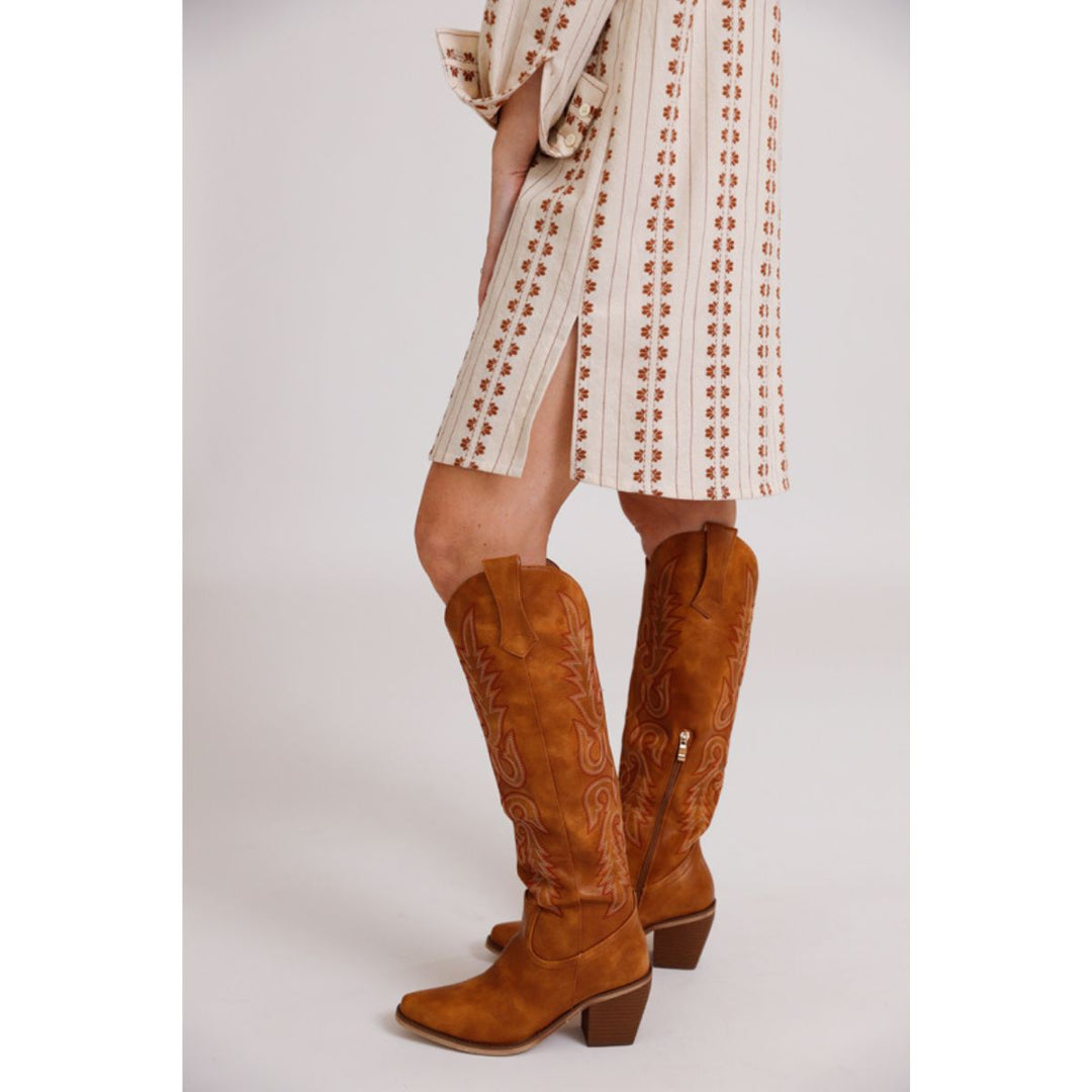 Brown knee-high boots worn with a patterned dress on a plain background