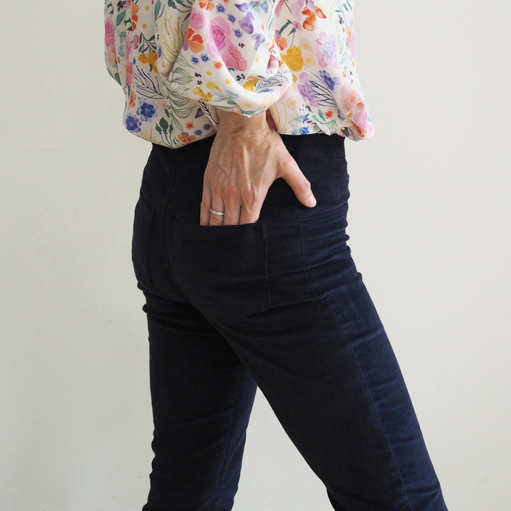 Model wearing the Eleonore trousers showing comfortable wide waistband and fitted hip shape, standing to the side with hand in back pocket