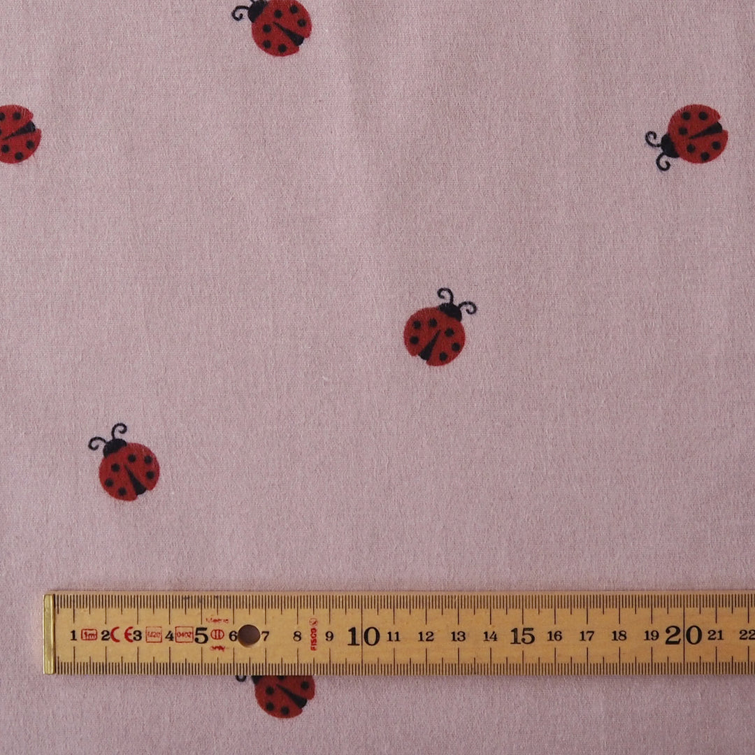 Ladybird Scatter Cotton Flannel Fabric with Red Ladybirds on a mauve pink background