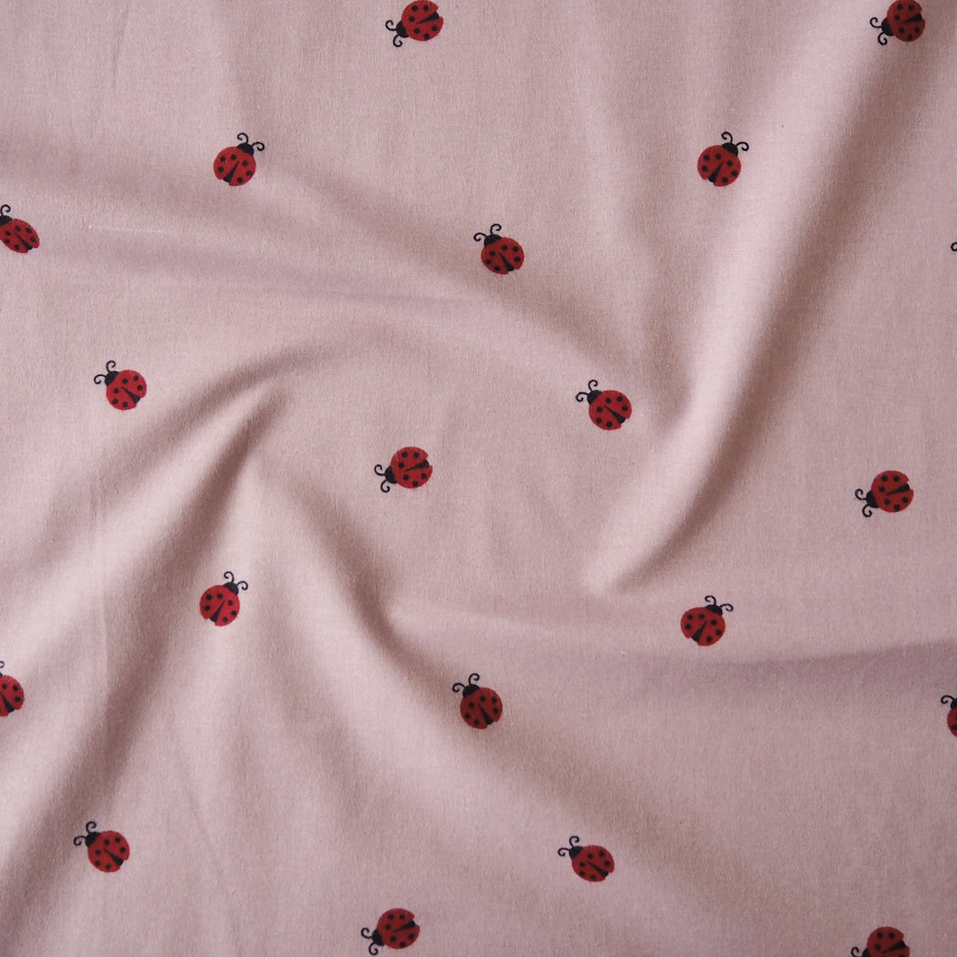 Ladybird Scatter Cotton Flannel Fabric with Red Ladybirds on a mauve pink background