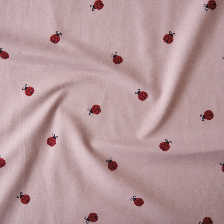 Ladybird Scatter Cotton Flannel Fabric with Red Ladybirds on a mauve pink background
