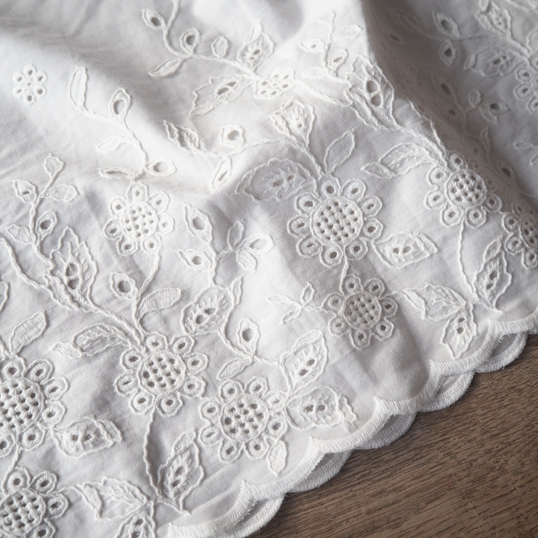 White cotton dressmaking fabric with floral embroidered border and scalloped edge