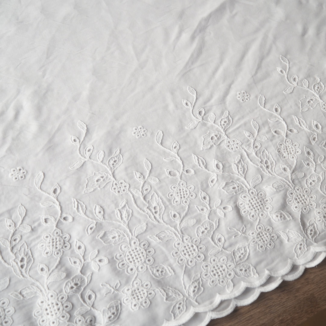 White cotton dressmaking fabric with floral embroidered border and scalloped edge