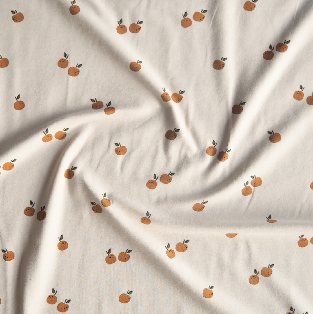 Ecru stretch cotton jersey dressmaking fabric with orange motifs