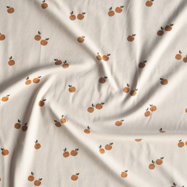 Ecru stretch cotton jersey dressmaking fabric with orange motifs