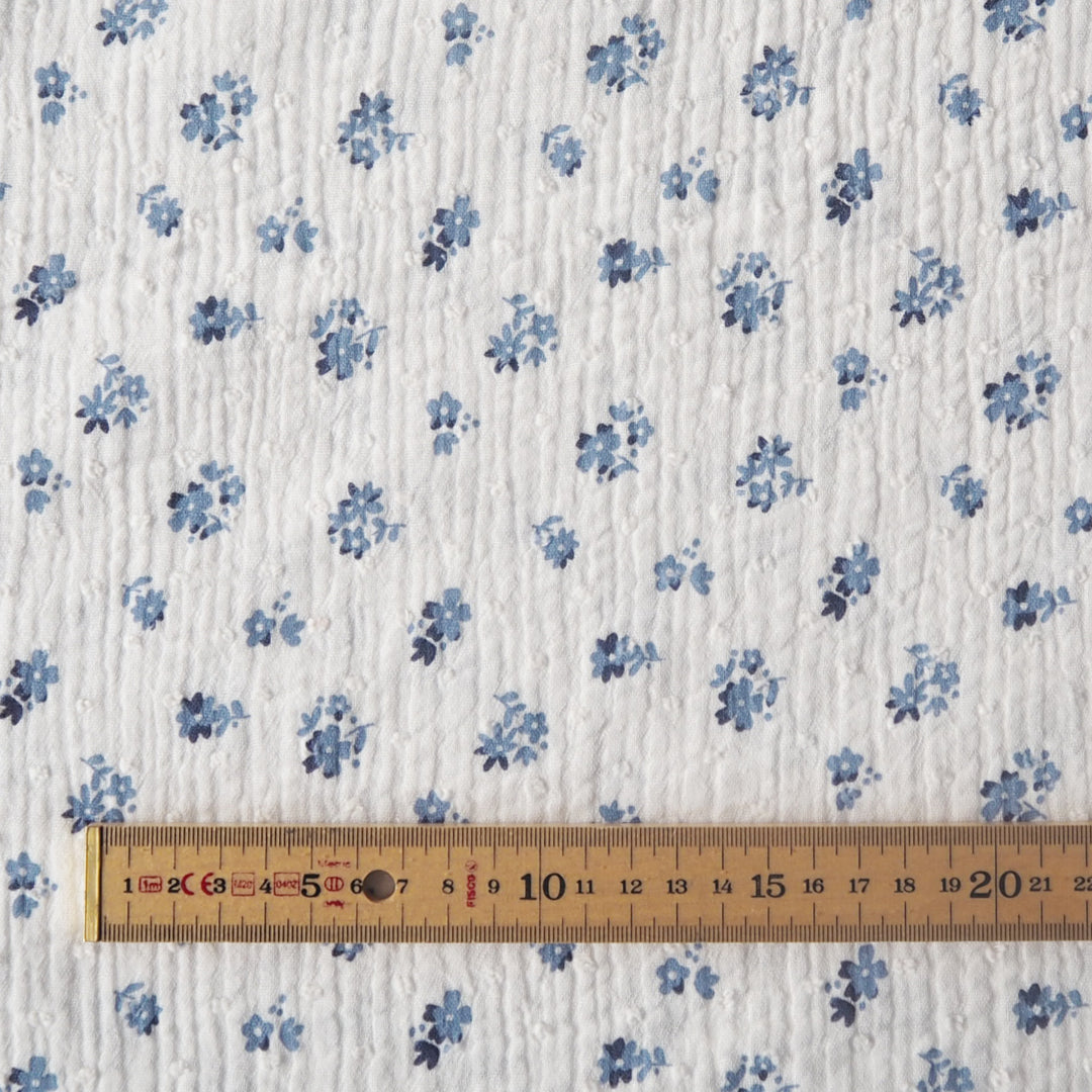 White cotton double gauze dressmaking fabric with dobby texture and ditsy blue floral pattern