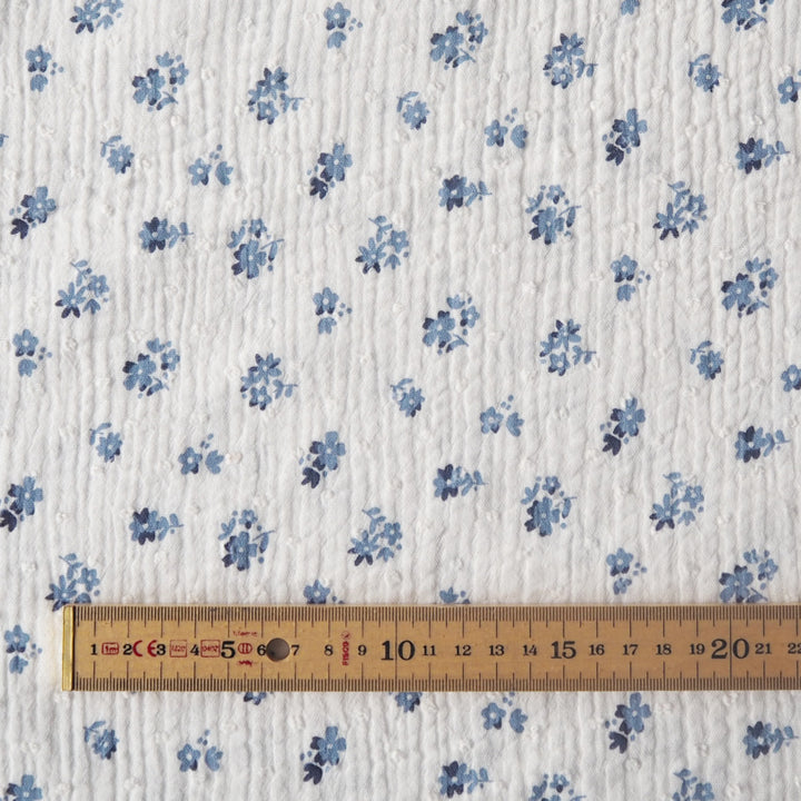White cotton double gauze dressmaking fabric with dobby texture and ditsy blue floral pattern