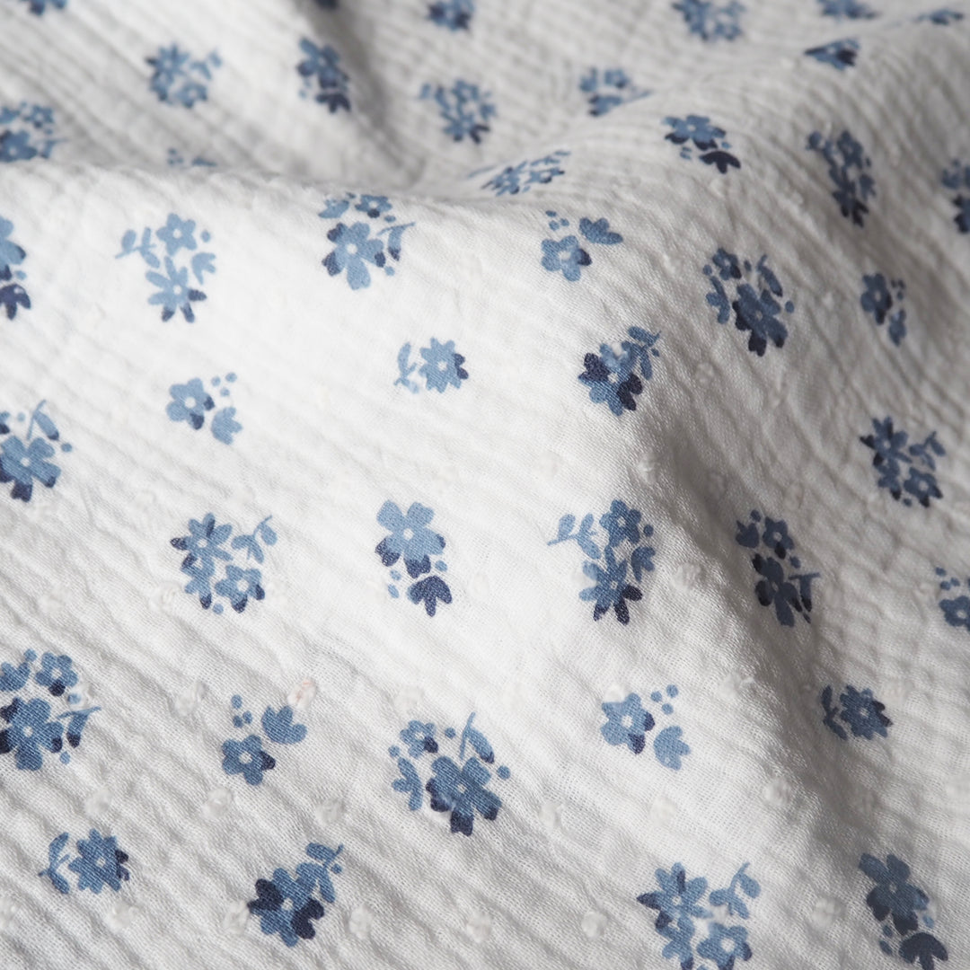 White cotton double gauze dressmaking fabric with dobby texture and ditsy blue floral pattern
