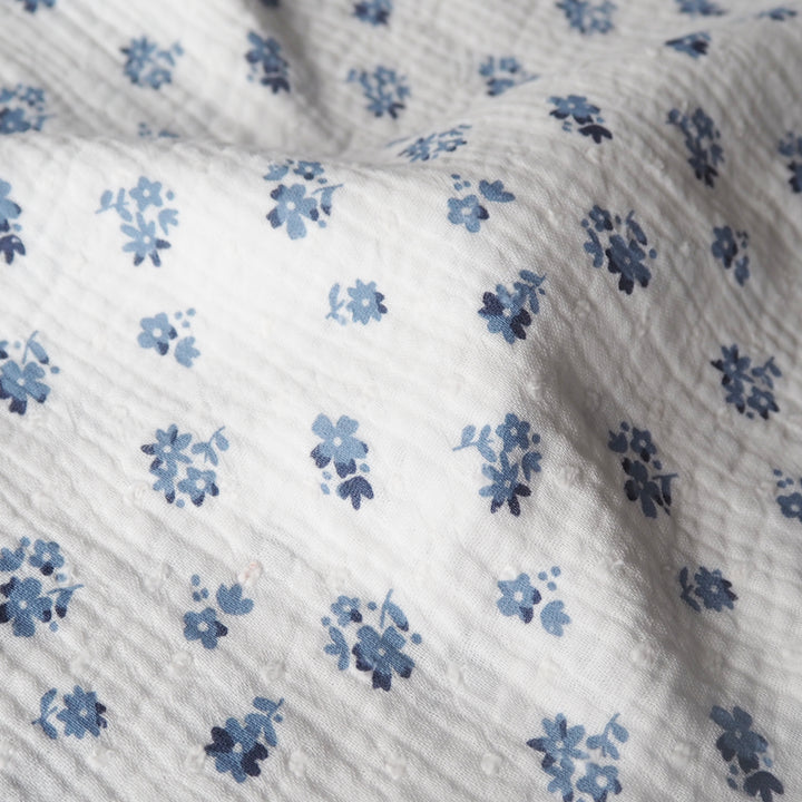 White cotton double gauze dressmaking fabric with dobby texture and ditsy blue floral pattern