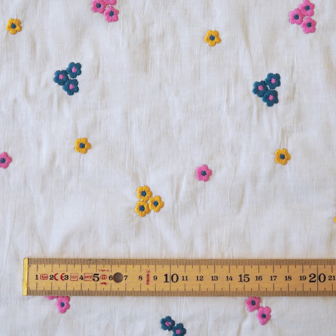White cotton voile fabric with small colourful embroidered flowers on a white background