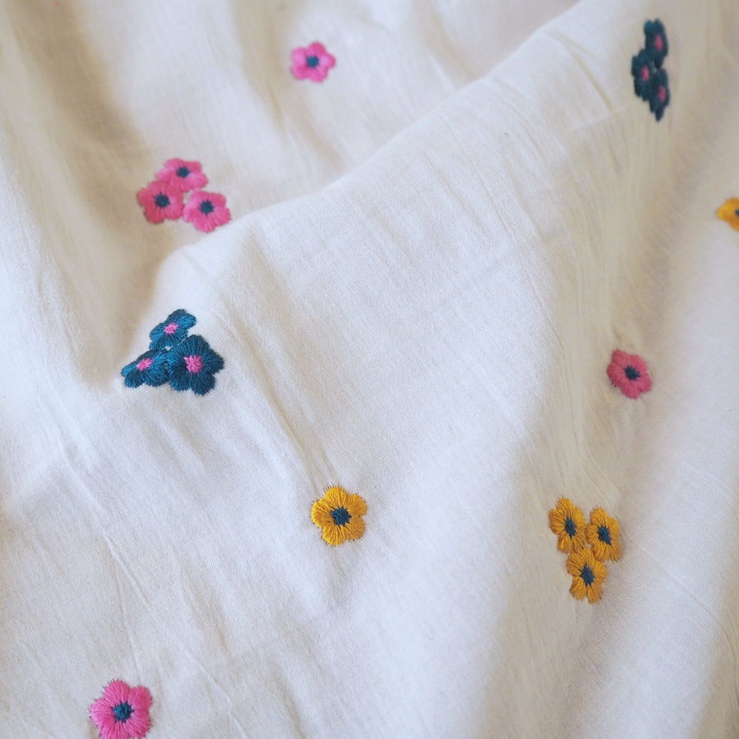White cotton voile fabric with small colourful embroidered flowers on a white background