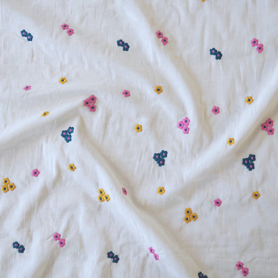 White cotton voile fabric with small colourful embroidered flowers on a white background