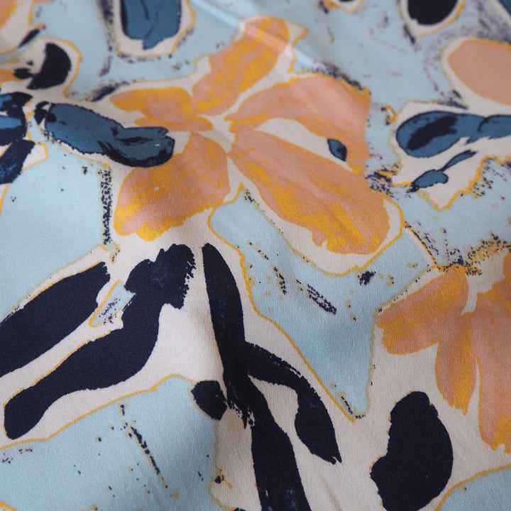 Floral patterned stretch cotton fabric with orange, blue, and black flowers on a light blue background