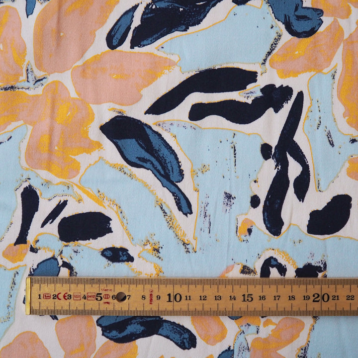 Floral patterned stretch cotton fabric with orange, blue, and black flowers on a light blue background