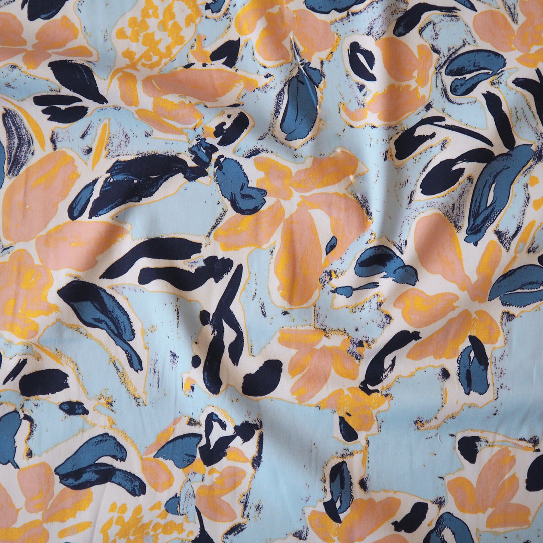 Floral patterned stretch cotton fabric with orange, blue, and black flowers on a light blue background