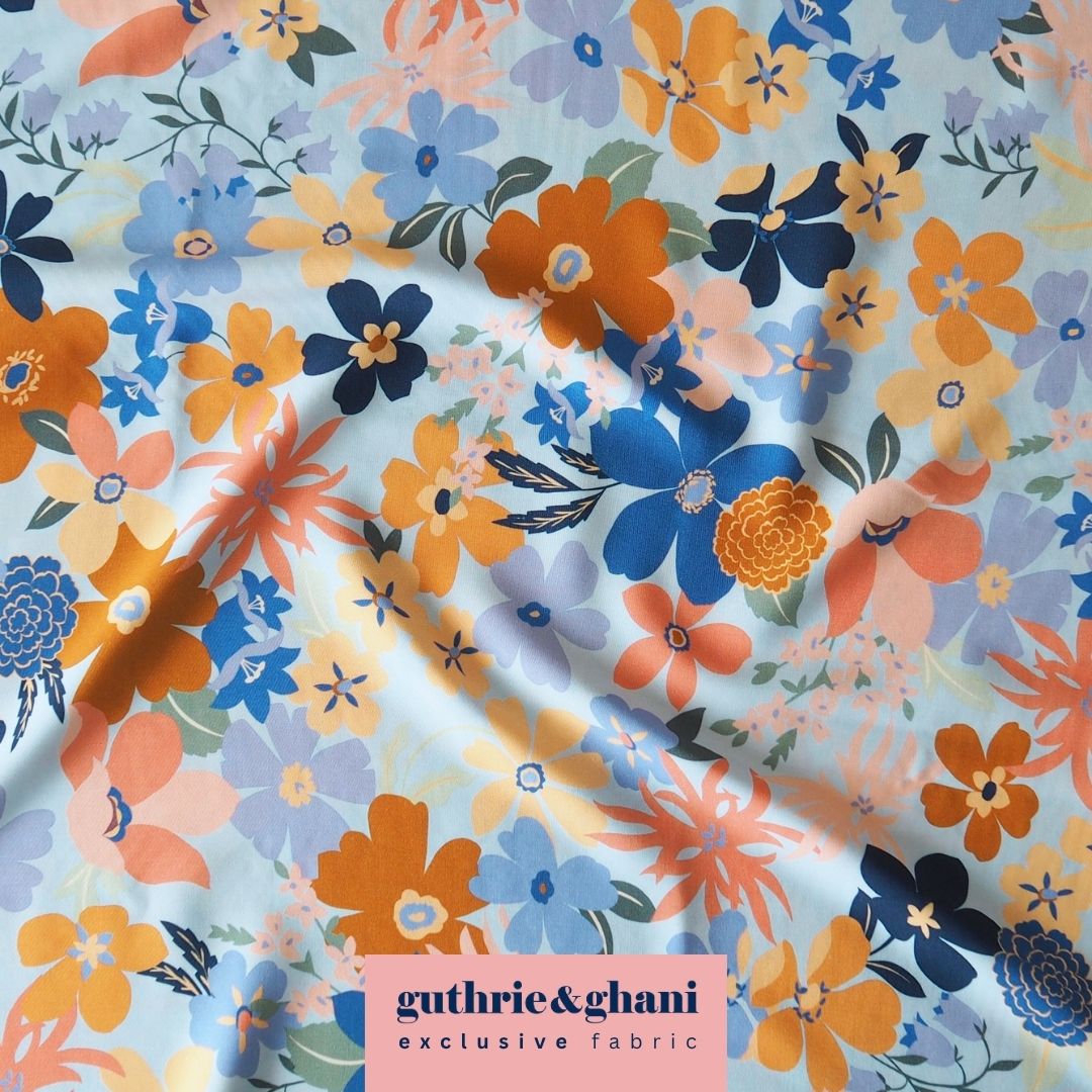 Floral fabric with orange, blue, and purple flowers on a light blue background, featuring the brand 'guthrie&ghani'.