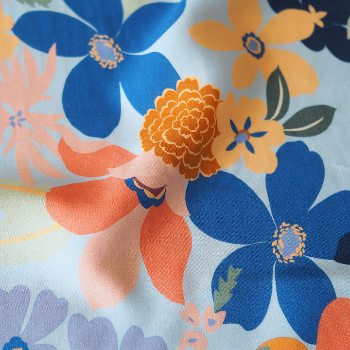 Close-up of colorful floral pattern with blue, orange, and purple flowers on a light background.