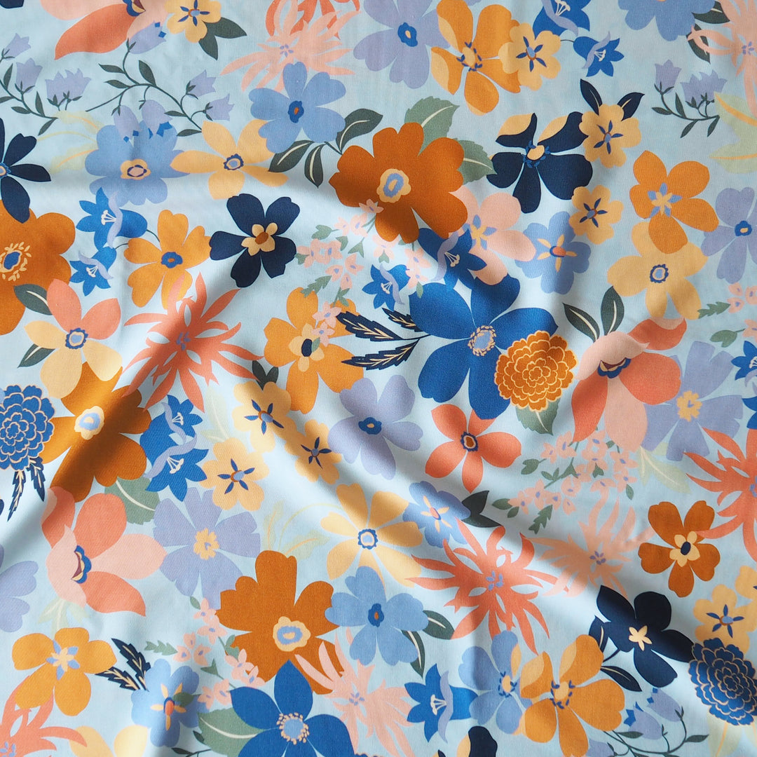 Floral fabric pattern with orange, blue, and purple flowers on a light blue background
